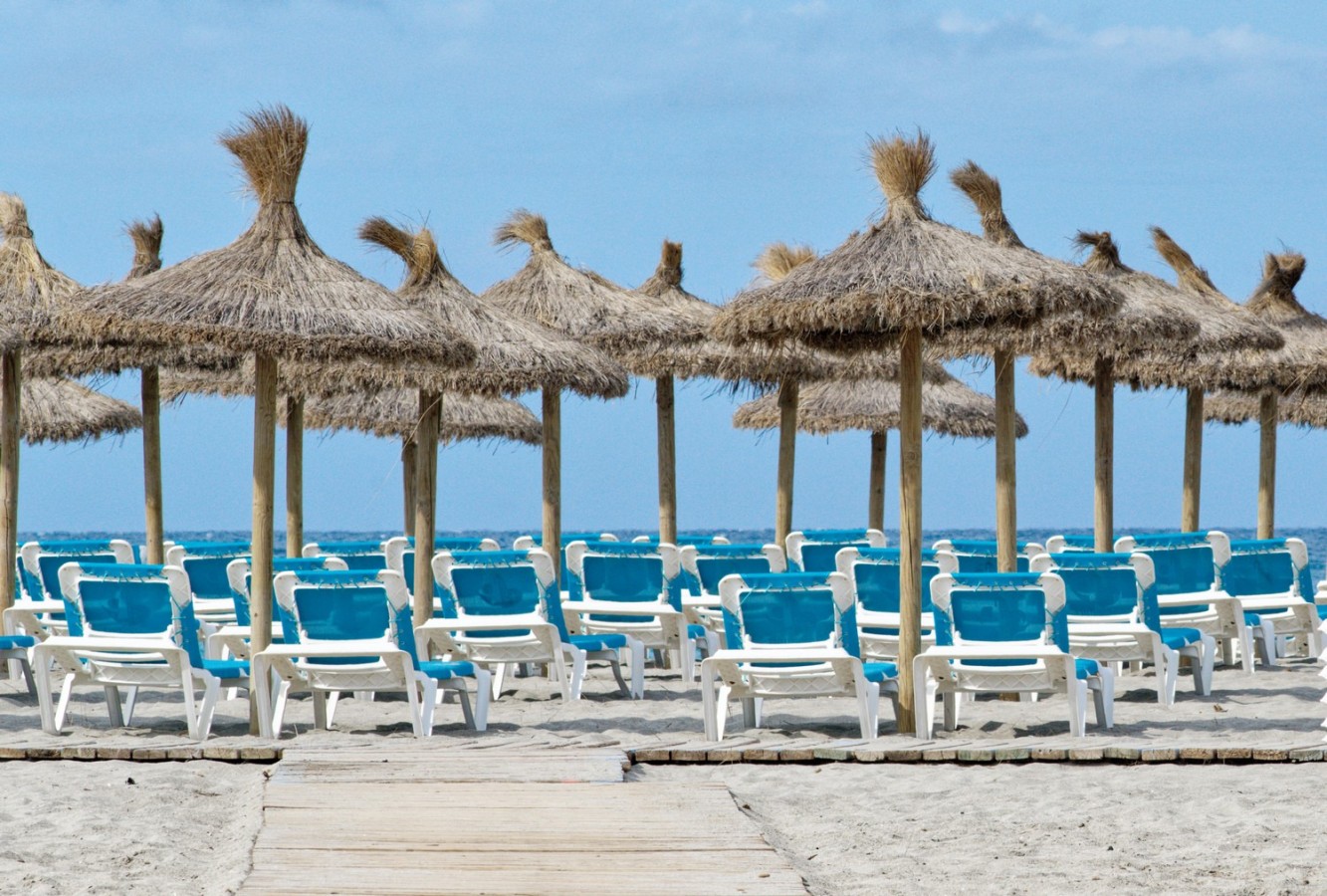 Strand mit Liegestühlen und Sonnenschirmen aus Stroh